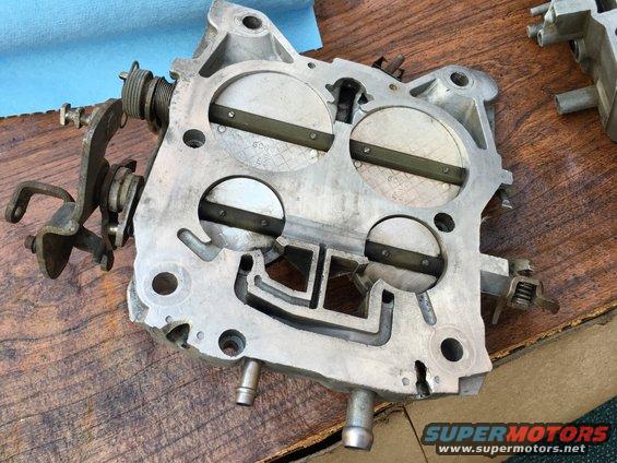 Close-up of a carburetor with four throttle plates. Some text is visible on the plates