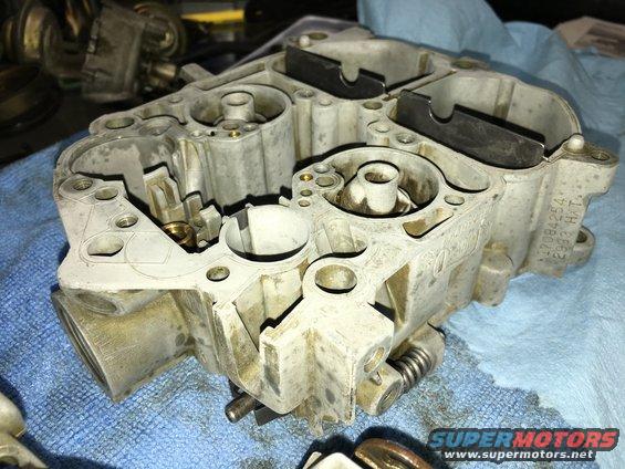 Carburetor part with visible casting numbers and springs, resting on a blue cloth