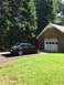 1967 Mercury Cougar - A dark sedan is parked on a paved driveway beside a brick garage on a sunny day.