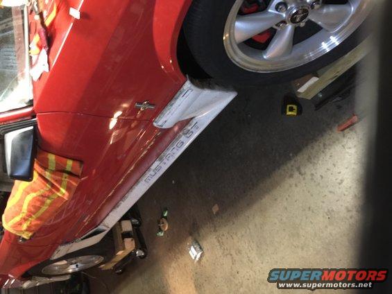 Red car side skirt with 'MUSTANG GT' text and a silver wheel