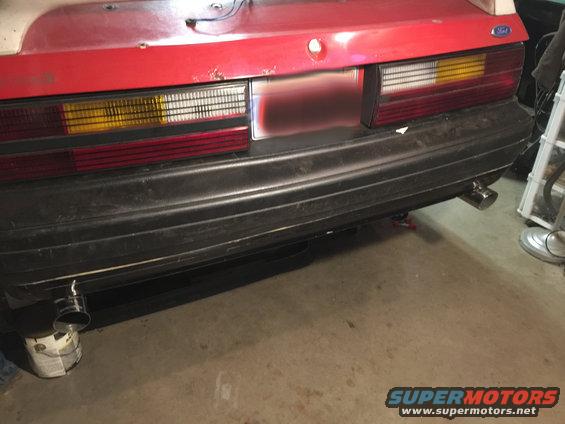Rear of a red 1983 Ford Mustang with black bumper and dual exhaust tips. Taillights are visible