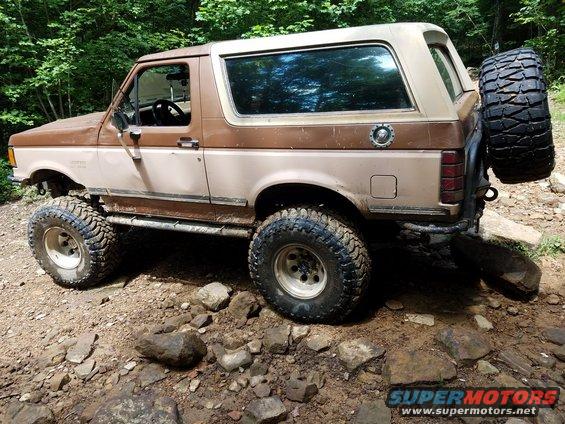Brown and tan Ford Bronco with lifted suspension and off-road tires, viewed from the front-left