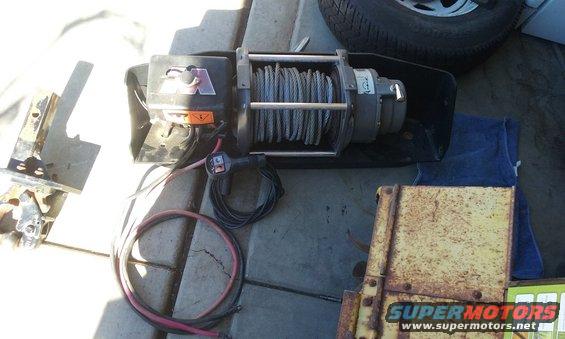 Winch with steel cable, remote control, and mounting bracket. Also a rusty yellow metal box