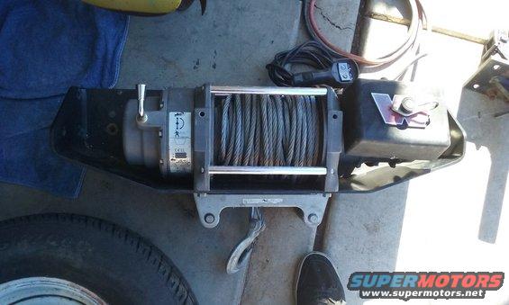 Winch with steel cable and red logo on black housing, mounted on a metal bracket