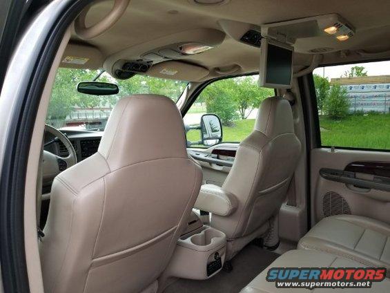 Inside of a large SUV, showing front leather seats, overhead console with a screen, and a rearview mirror