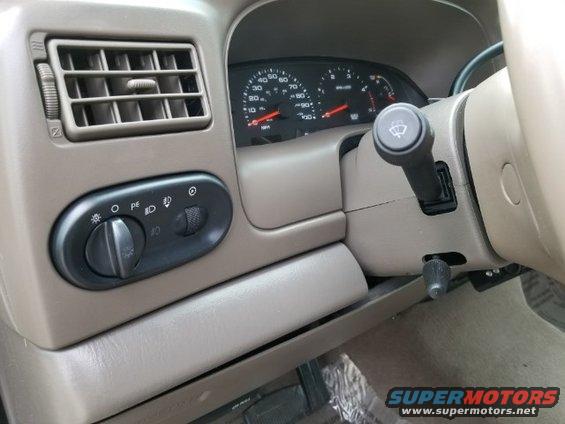 Dashboard interior with air vent, headlight controls, and instrument cluster. Beige dashboard
