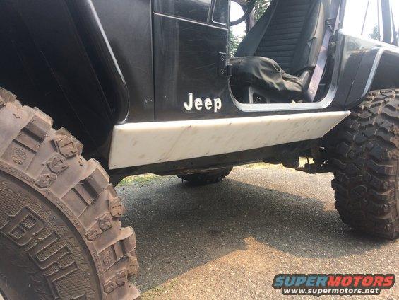 Side view of a black 1995 Jeep YJ with white rocker protection and large off-road tires