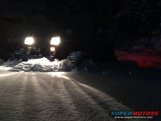 1995 Jeep Wrangler driving through snow at night, headlights on