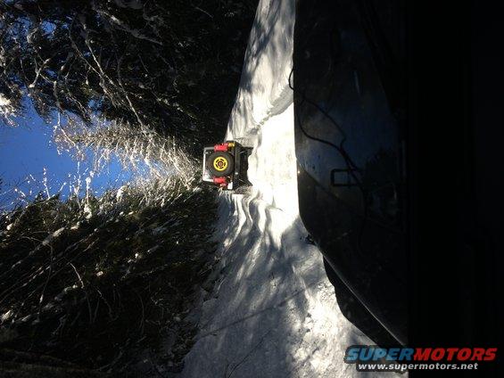 Off-road vehicle with yellow spare tire cover on snowy path, trees on left