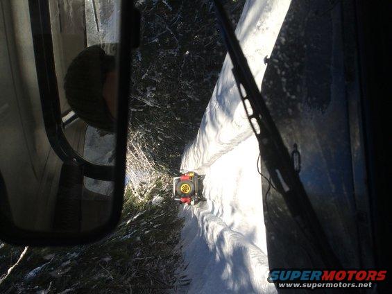 View from inside a vehicle looking out at a small yellow vehicle driving on a snowy path