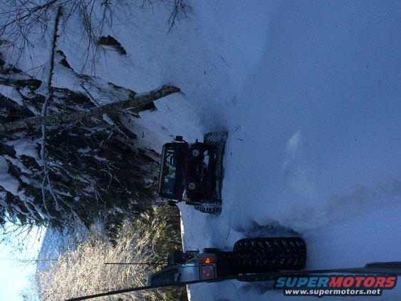 Two off-road vehicles navigate a snow-covered trail with trees on the left
