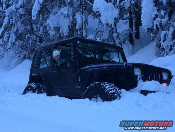 Black 1995 Jeep YJ stuck in deep snow, driver visible