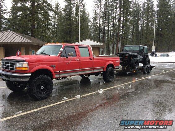 Red Ford F-Series truck towing a black Jeep Wrangler on a trailer