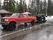 1995 Jeep YJ - A red Ford F-Series truck tows a black Jeep Wrangler on a trailer in a snowy, wet parking lot.