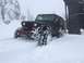 1995 Jeep YJ - A Jeep Wrangler navigates through a snowy landscape, with trees and a building visible in the background.