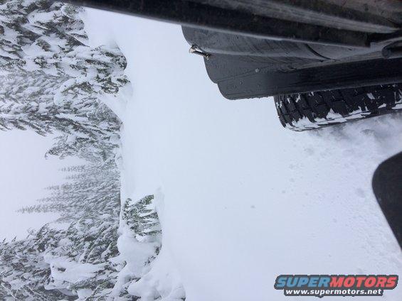 vehicle driving through deep snow next to snow-covered trees
