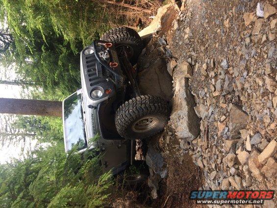 Silver Jeep Wrangler Rubicon on a rocky trail, tires angled on rocks. Rubicon text visible on fender