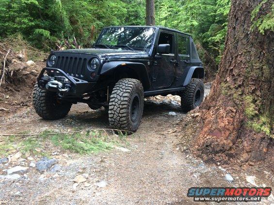Black Jeep Wrangler with aftermarket bumper and winch on a dirt trail