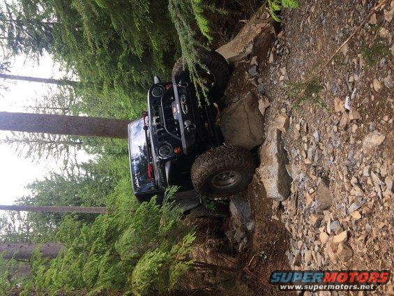 Black 1995 Jeep YJ navigating a steep, rocky trail with trees on either side