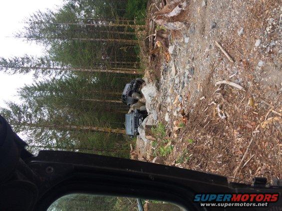 Two dark-colored Jeeps navigating a rocky, wooded trail