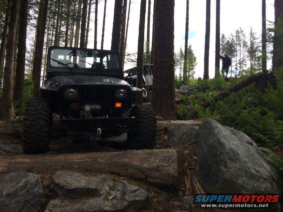 Black Jeep Wrangler on a rocky, wooded trail with large tires and a winch