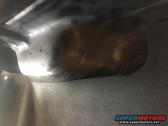 Underside of a dark-colored car part with visible texture and a small hole