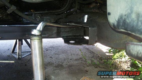 Car frame supported by jack stands, with a hydraulic jack and wrench attached to a bolt
