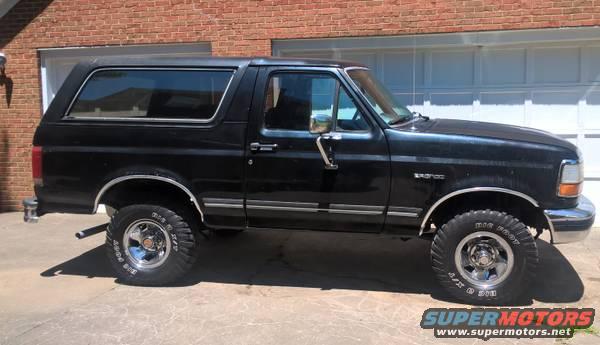 Black Ford Bronco with chrome wheels parked in front of a garage
