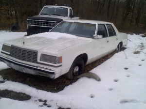 White sedan parked in snow with a pickup truck behind it