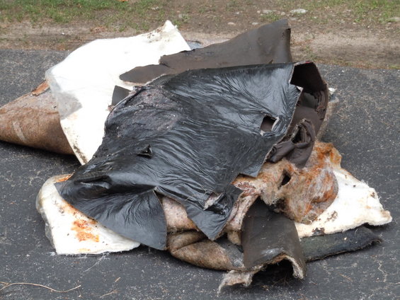 Pile of ripped insulation and black plastic sheeting on asphalt