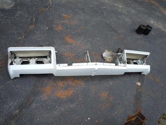 White front bumper assembly with headlight housings removed, lying on asphalt