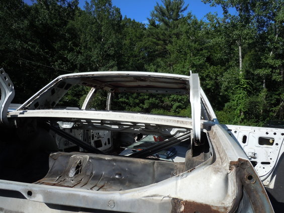 car body stripped down to frame, doors open, rust visible