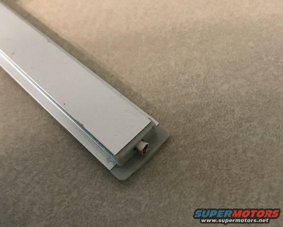 White plastic trim piece with exposed red and white wires, on a textured surface