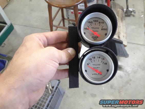 Dual gauge cluster with red needles, one labeled DIFF TEMP and the other VOLTS, held by a hand