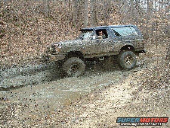 1987 Ford Bronco driving through mud on a wooded trail
