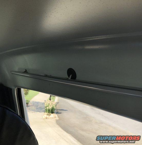 Interior view of a vehicle's gray headliner and window frame, looking out at a driveway and bushes