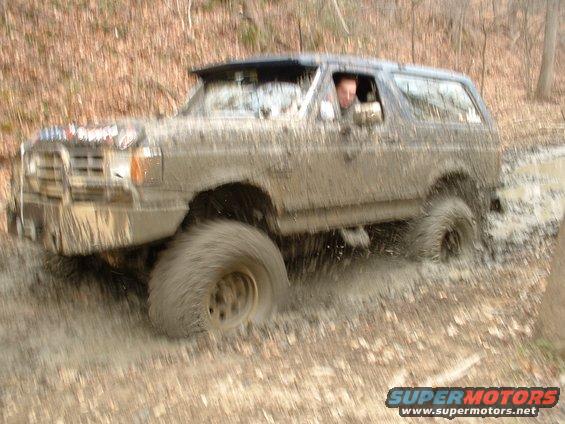 Muddy SUV driving through a puddle, driver visible