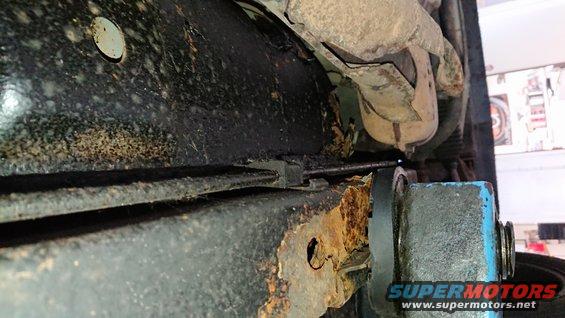 Undercarriage frame with extensive rust and black undercoating. A cable runs along the frame
