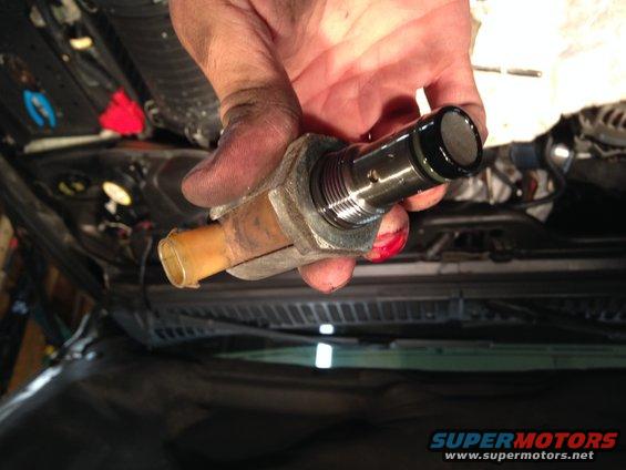 Hand holding a dirty oil pressure sensor with a plastic tube fitting