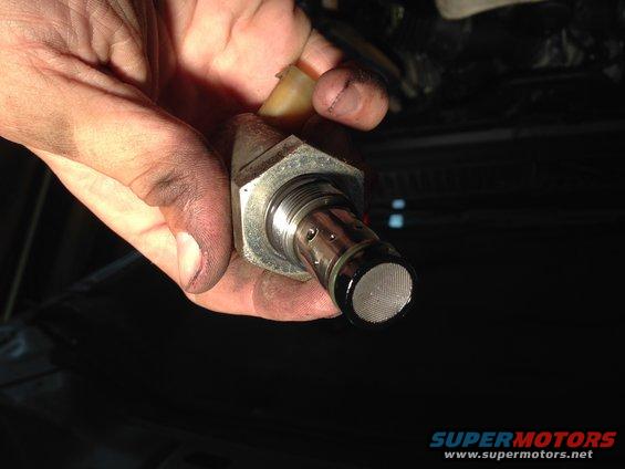 Hand holding a fuel pressure regulator with a mesh filter