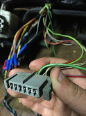 Hand holding gray wiring harness connector with many colored wires