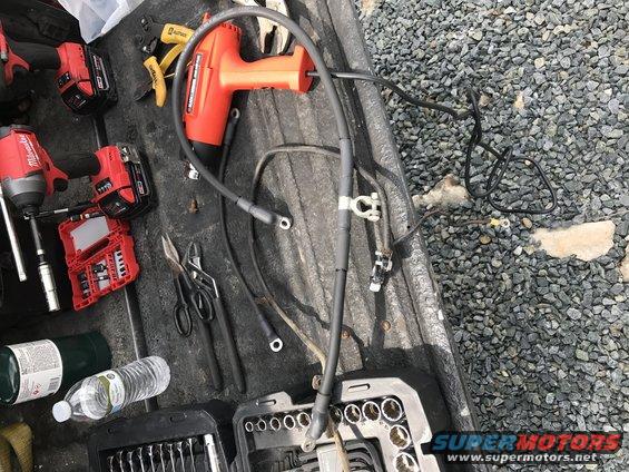 Battery cables, impact wrench, pliers, and a socket set laid out in a truck bed