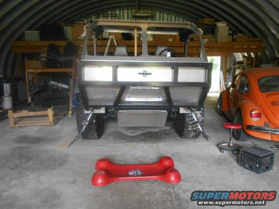 Custom off-road vehicle chassis in a garage with an orange Volkswagen Beetle parked nearby