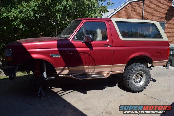 Red Ford Bronco SUV with tan trim, lifted, on jack stands, with large tires