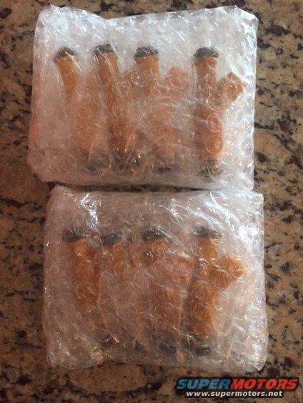Two sets of four orange fuel injectors wrapped in bubble wrap