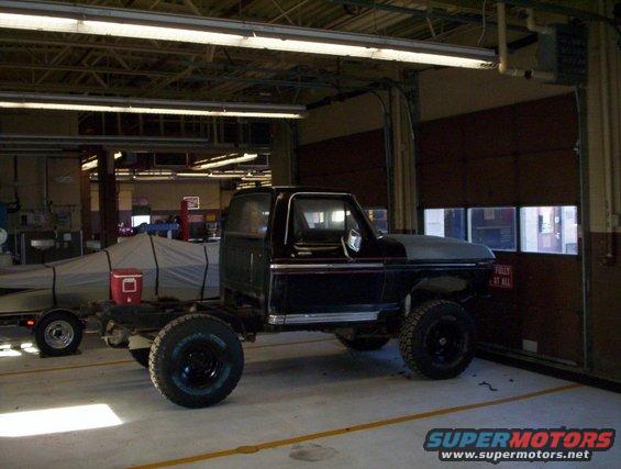 Truck chassis with a boat on a trailer behind it in a garage