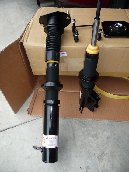 Two black car shock absorbers and mounting hardware on a cardboard box