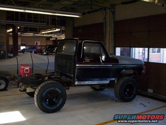 Black Ford F-Series truck chassis with a bare hood, viewed from the front-right in a garage
