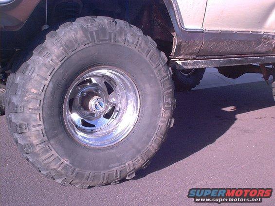 Close-up of a large off-road tire on a chrome rim, showing the side of a vehicle with dark lower body panels