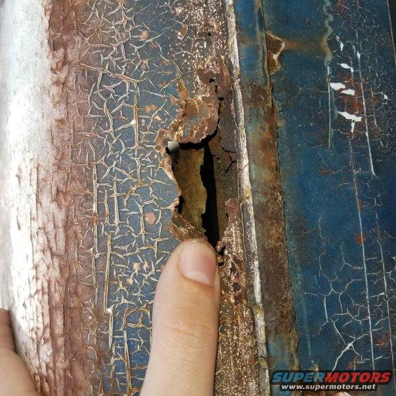 Rust hole in blue paint with cracked finish
